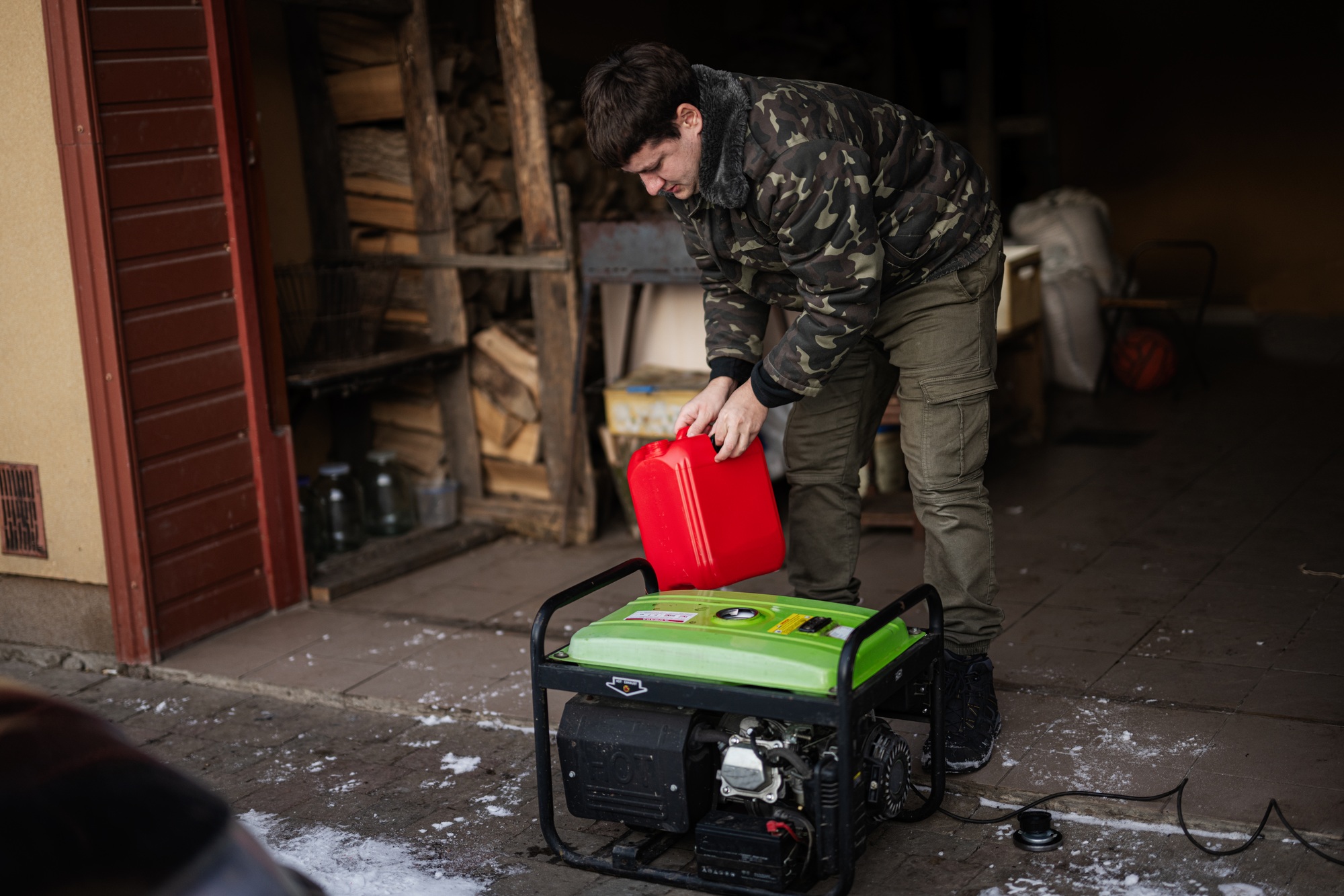 Man wear in military jacket pour gasoline from canister in portable mobile backup standby generator.